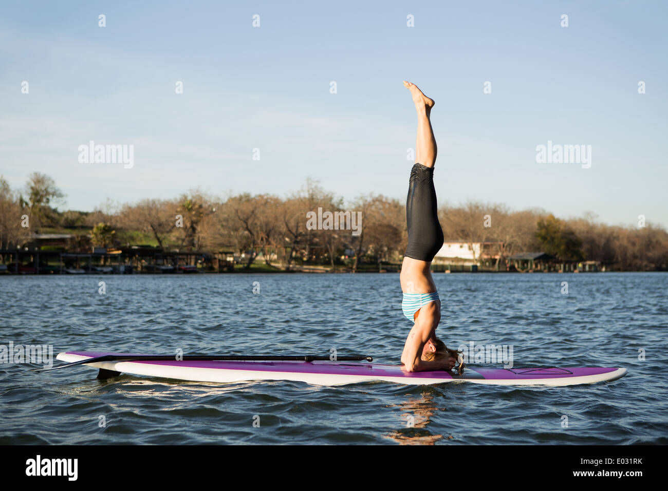 Eine Frau macht einen Kopfstand auf einem Paddle Board auf See Stockfoto