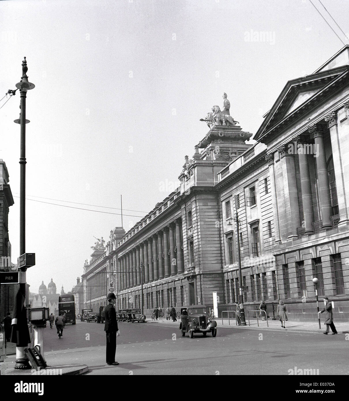 1950 s, historischen, einen Blick auf das Grand Victorian columed Gebäude in Kingston upon Hull City Centre als Polizist den Verkehr lenkt. Wir sehen die Autos der Epoche und einer Aktiengesellschaft Motorbus Transport Doppeldecker in der Ferne. Stockfoto