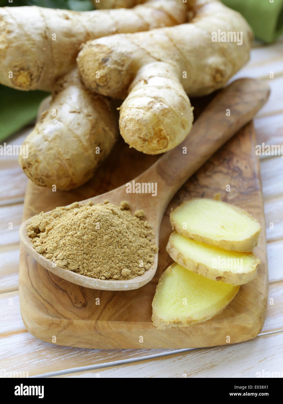 gemahlener Ingwer in einem hölzernen Löffel, frische Wurzel im Hintergrund Stockfoto