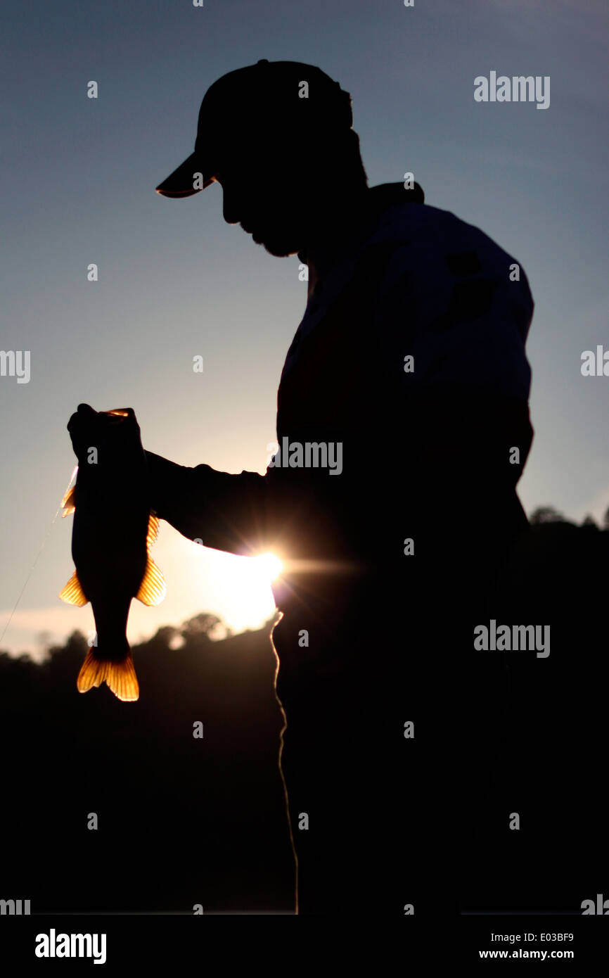 Ein einsamer Bass Angler bewundert die endgültige Largemouth des Tages als die Sonne hinter den Hügeln am Lake Berryessa in Kalifornien. Stockfoto