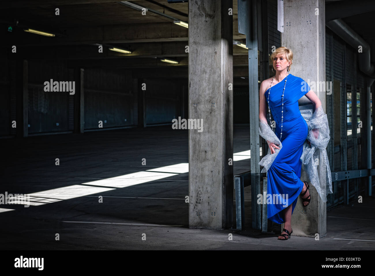 Schöne Reife Frau trägt blaue Kleid und posiert im öffentlichen Parkhaus Stockfoto