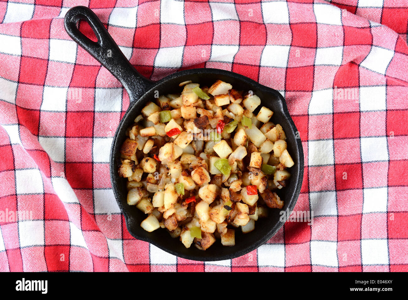 Hohen Winkel Schuss von einer gusseisernen Pfanne mit Kartoffeln O'brien auf einer roten aufgegebenes Tischdecke. Stockfoto