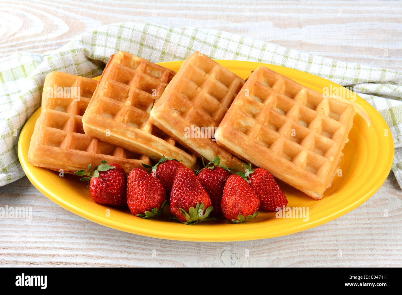 Ein Teller mit Waffeln und Erdbeeren auf einer gelben Platte. Querformat auf einem rustikalen hölzernen Bauernhaus Stil Tisch. Stockfoto