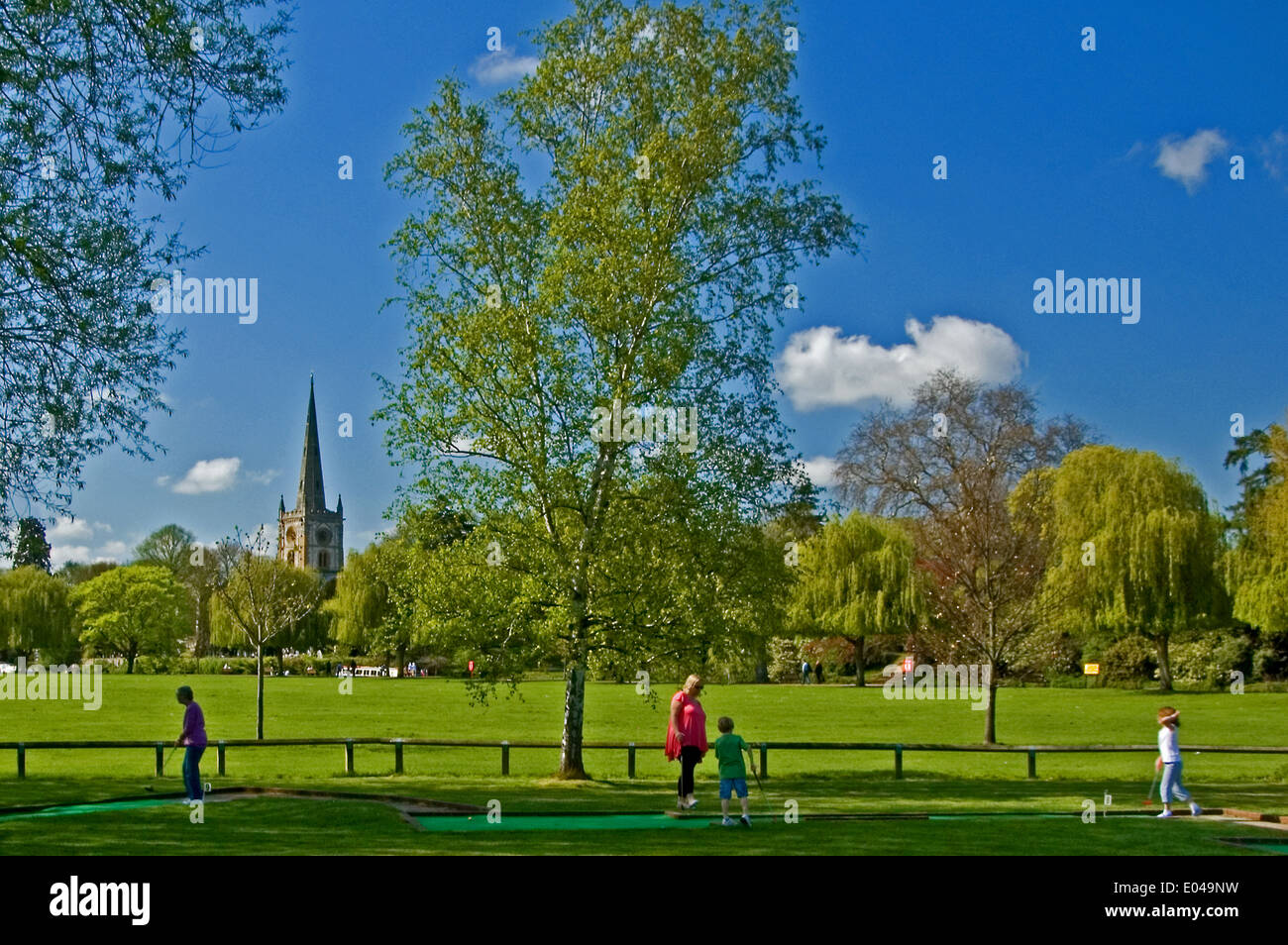 Familiengruppe spielen Minigolf in Stratford-upon-Avon, Heilige Dreifaltigkeit Kirchturm steht über den Bäumen. Stockfoto