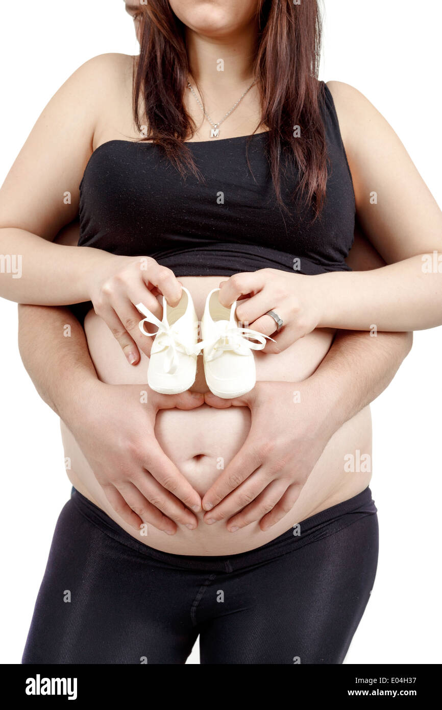 Schwangere Frau mit einem Kind Schuh, ihr Mann zärtlich hält ihren Bauch mit Herzform Stockfoto