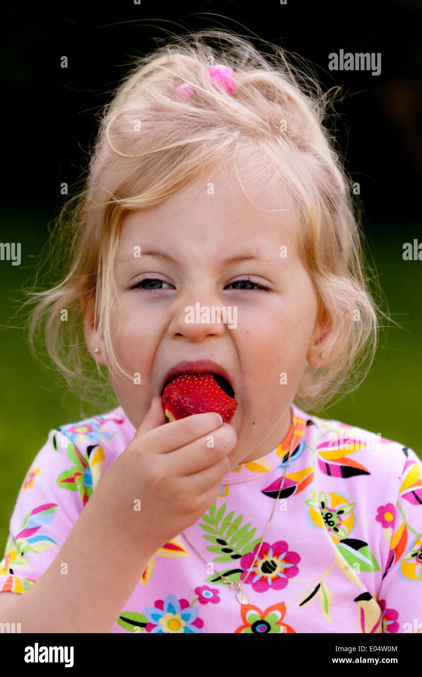 Kleines Kind mit Lebensmitteln eine Erdbeere in den Wachen, kleine Art Beim Essen Einer Erdbeere Im Garten Stockfoto