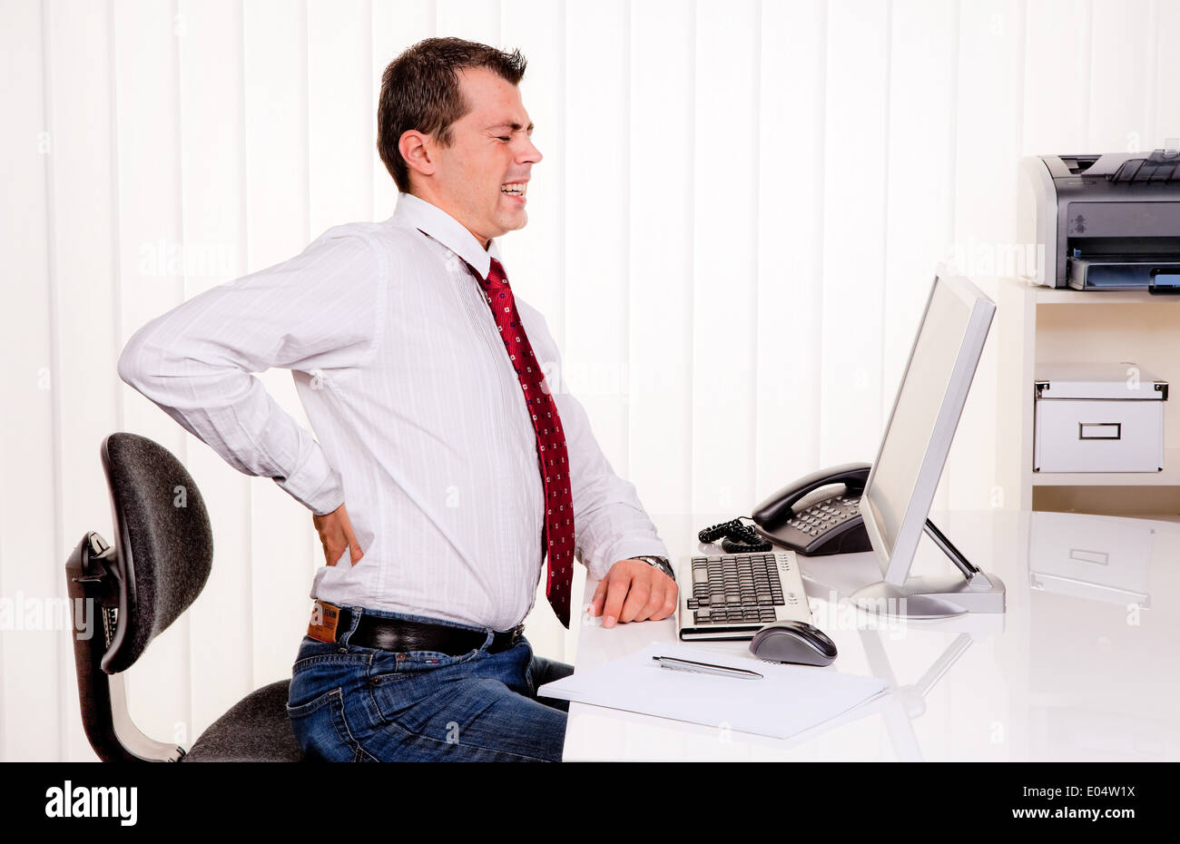 Young man im Büro von Computer und Rückenschmerzen Stockfoto