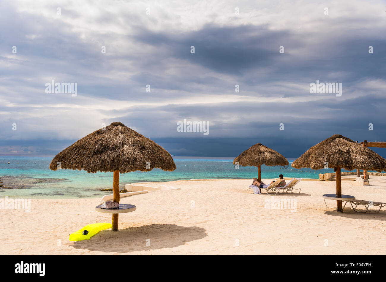 Strohgedeckte Sonnenschirme am Strand unter bewölktem Himmel. Cozumel, Mexiko. Stockfoto