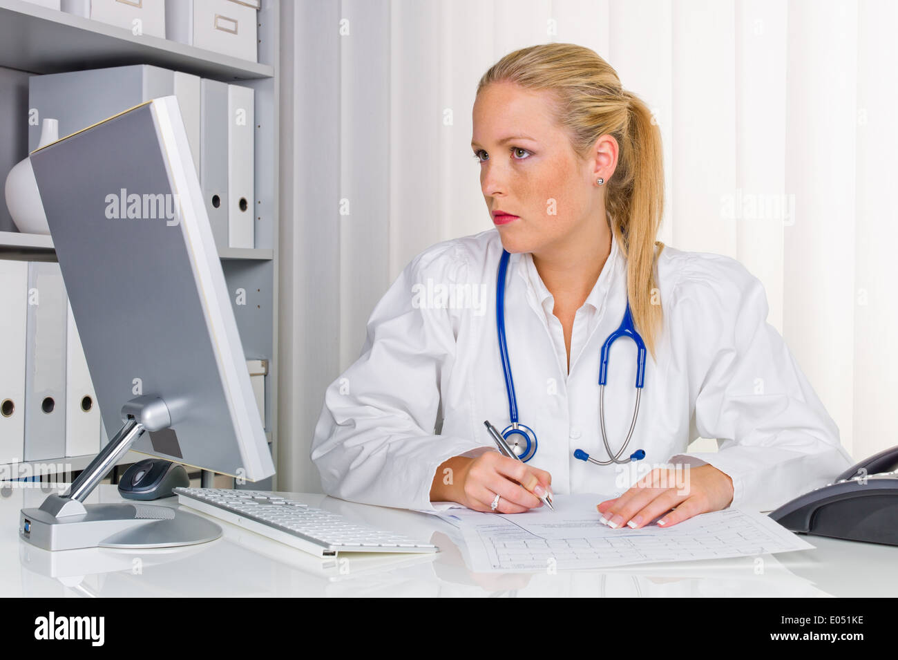Ein junger Arzt mit Stethoskop in ihrer medizinischen Praxis, Eine Junge √Ñrztin Mit Stethoskop in Ihrer Arztpraxis. Stockfoto