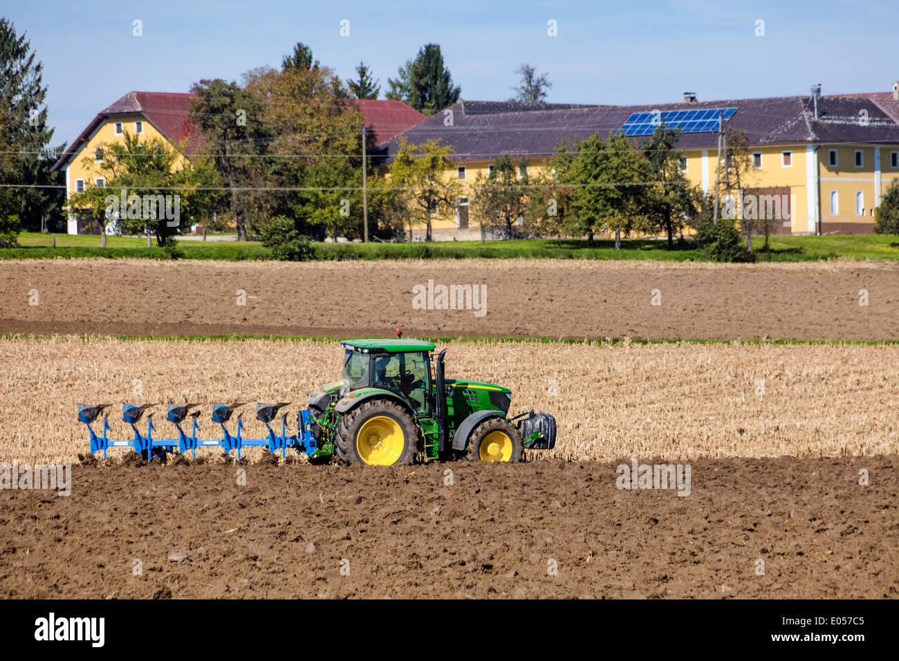 Ein Traktor auf einem Feld mit Pflügen. Im Hintergrund ein Bauernhaus, Ein Traktor Auf Einem Feld Beim Pfluegen. Im Hintergrund Ein Ba Stockfoto