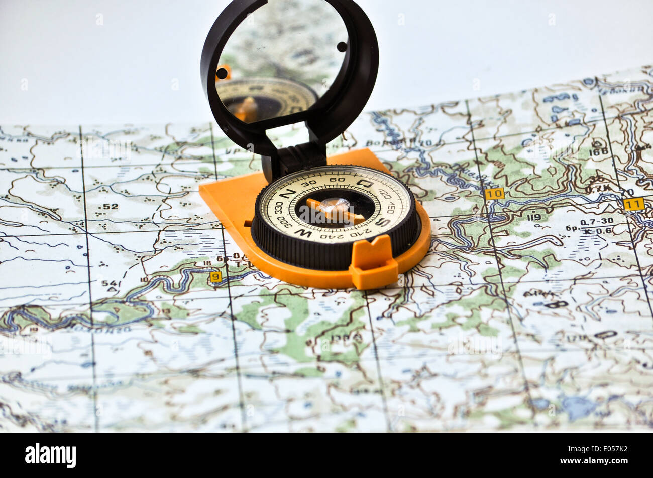 Topographische Karte liegt auf einem weißen Hintergrund, und es gibt ein magnetischen Kompass in einem schwarzen Kasten auf eine orange Boden. Stockfoto
