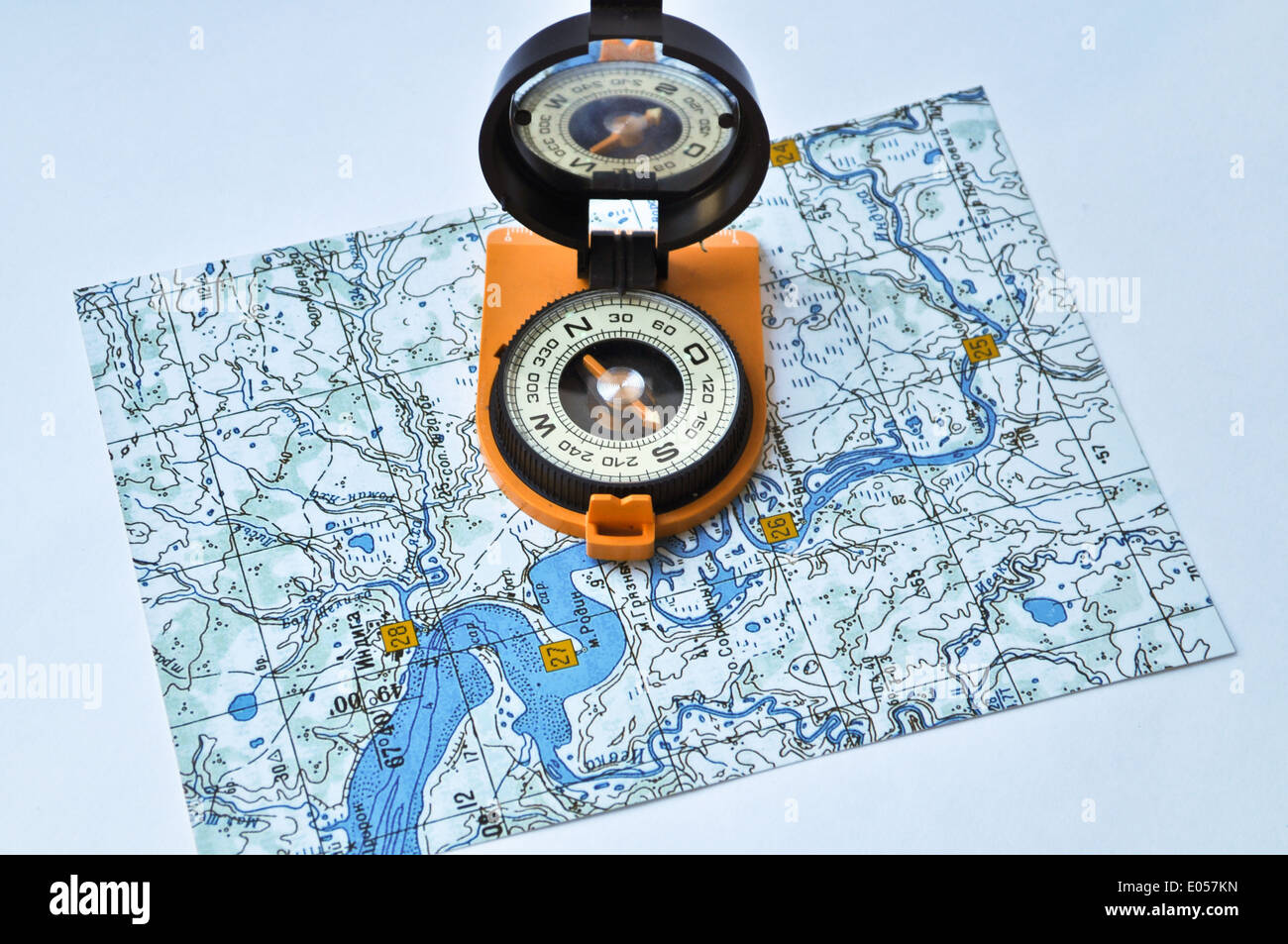 Topographische Karte liegt auf einem weißen Hintergrund, und es gibt ein magnetischen Kompass in einem schwarzen Kasten auf eine orange Boden. Stockfoto