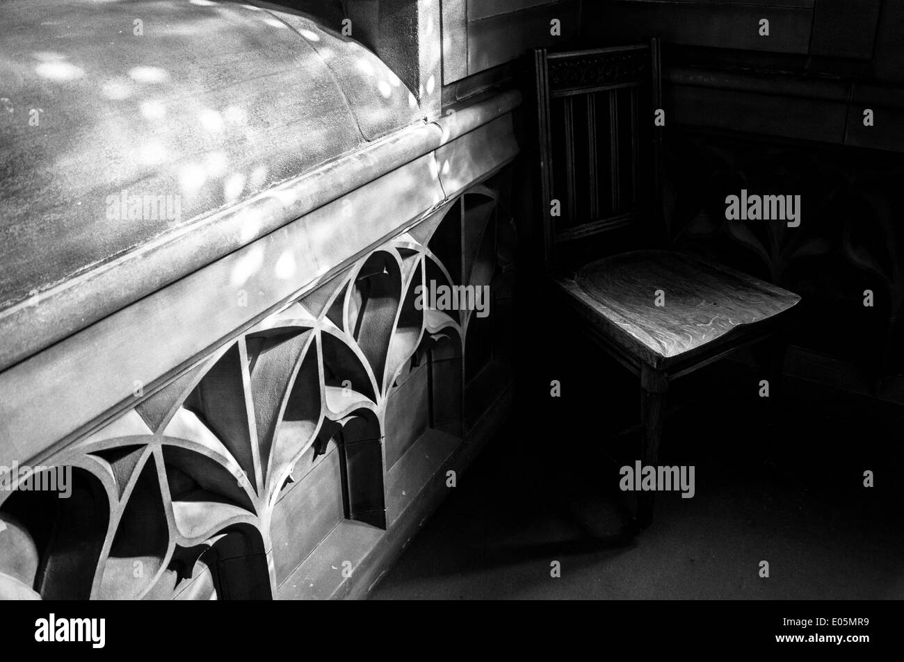 Holzstuhl teilweise im tiefen Schatten befindet sich innerhalb einer gotischen Sandstein-Bibliothek. Schatten sind tief & Lichtspiele auf dem Stein. Stockfoto