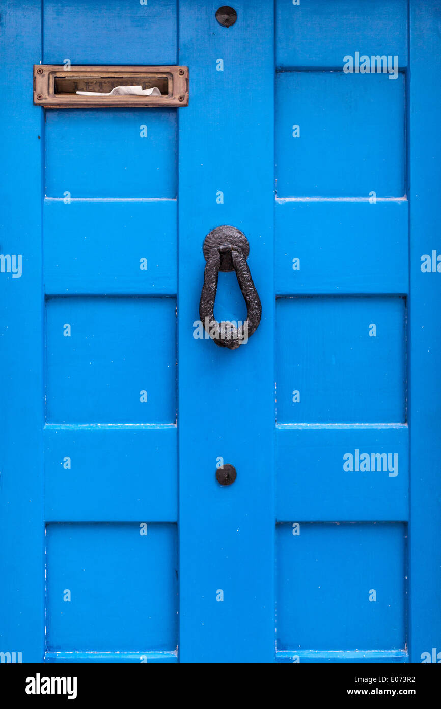 eine blaue Holztür mit einem Türklopfer und einen vollen Briefkasten Stockfoto