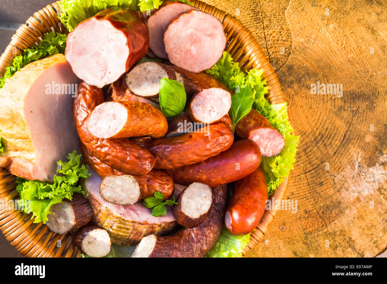 Verschiedene Fleisch- und Wurstwaren in einem Korb auf einem Holztisch Stockfoto