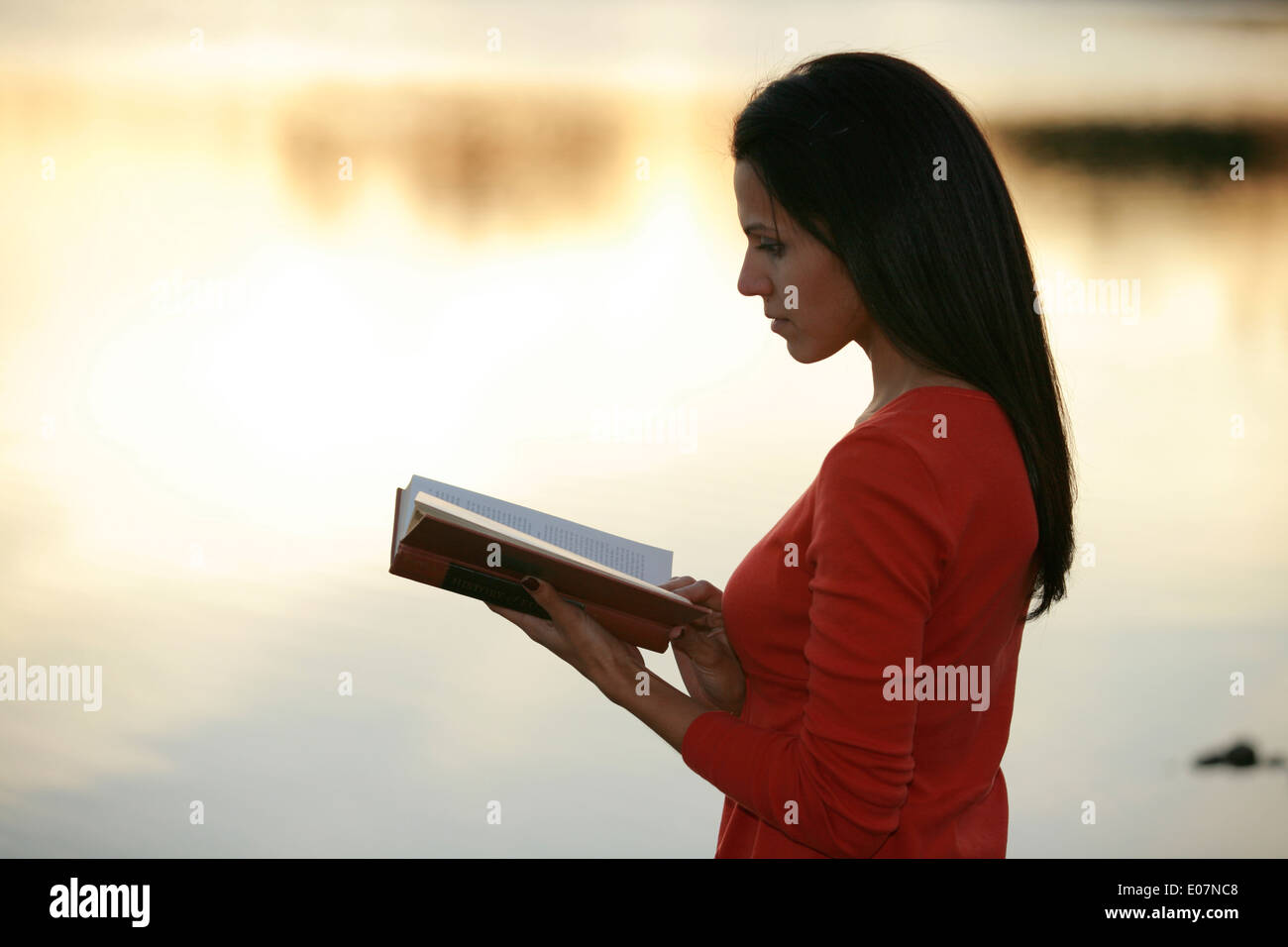 Schöne junge lateinamerikanische Frau Modell liest im Freien an einem Herbstabend am Ufer eines Sees. Stockfoto
