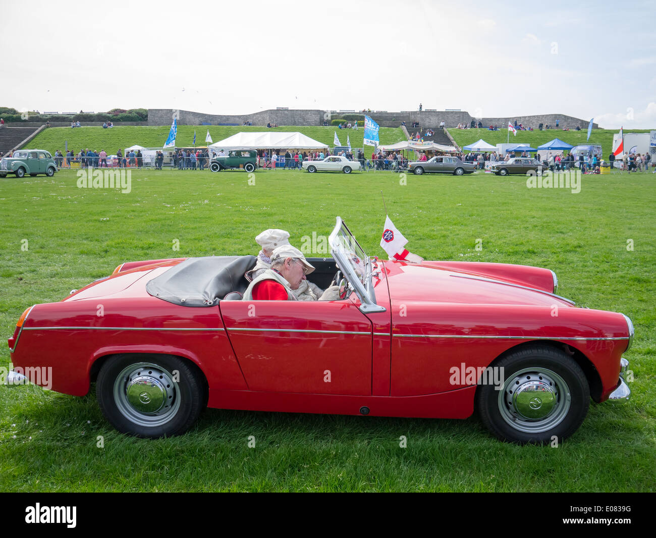 Ein Mann fährt einen roten 1962 Mk1 MG Midget mit einem weiblichen Passagier Stockfoto
