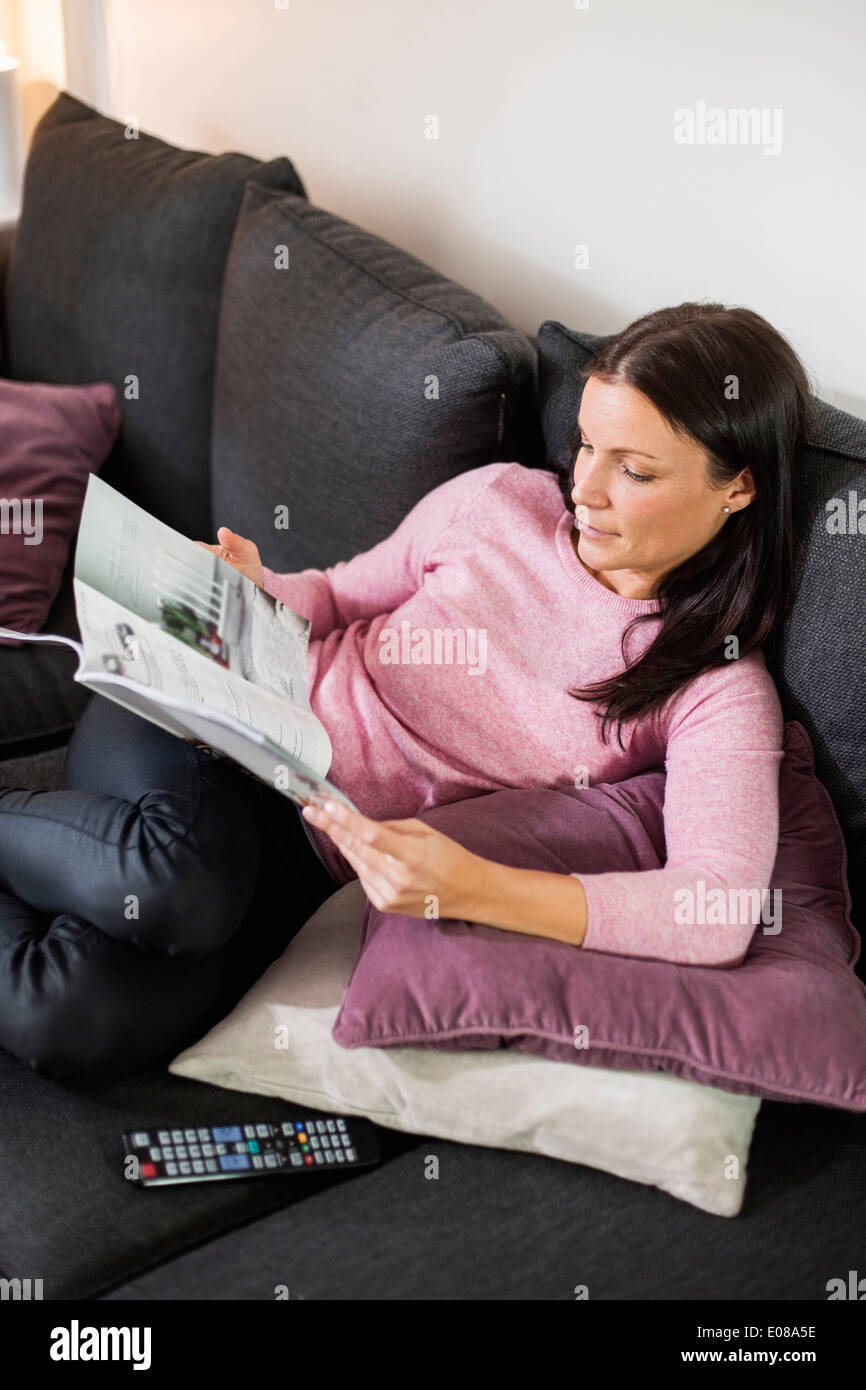 Mitte Erwachsene Frau lesen Magazin, während Sie gemütlich auf dem Sofa zu Hause Stockfoto