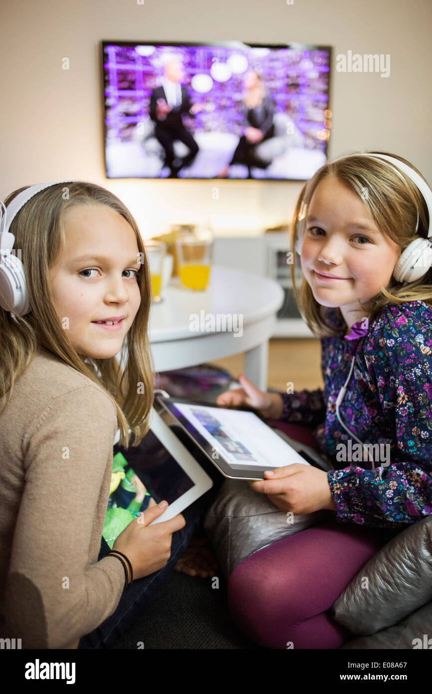 Porträt von lächelnden Schwestern hören Musik auf digitale Tablets im Wohnzimmer Stockfoto