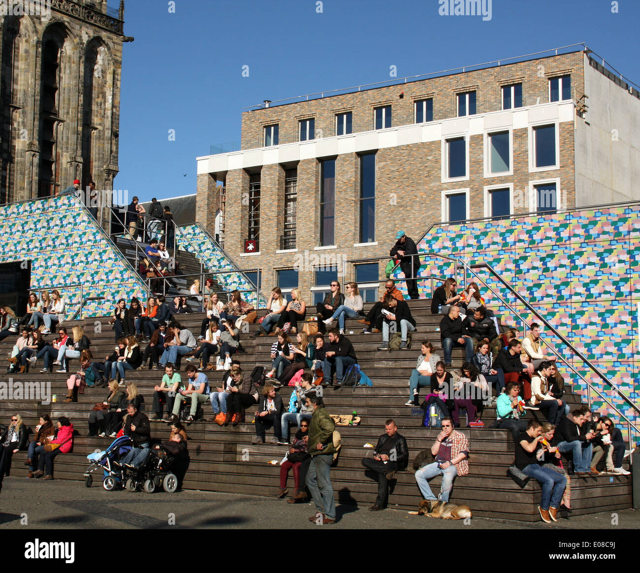 Menschen genießen die Frühlingssonne auf der Treppe des Fremdenverkehrsamtes auf dem Hintergrund der neuen Schüler-Gesellschaft in Groningen Stockfoto