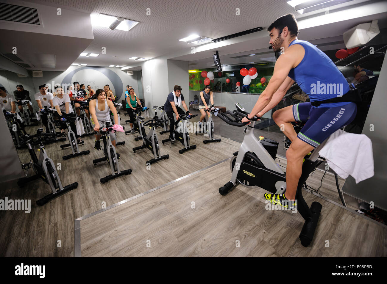Fitness-Trainer vor Menschen auf stationären Fahrrädern während einem Spinning Kurs in der Turnhalle Stockfoto