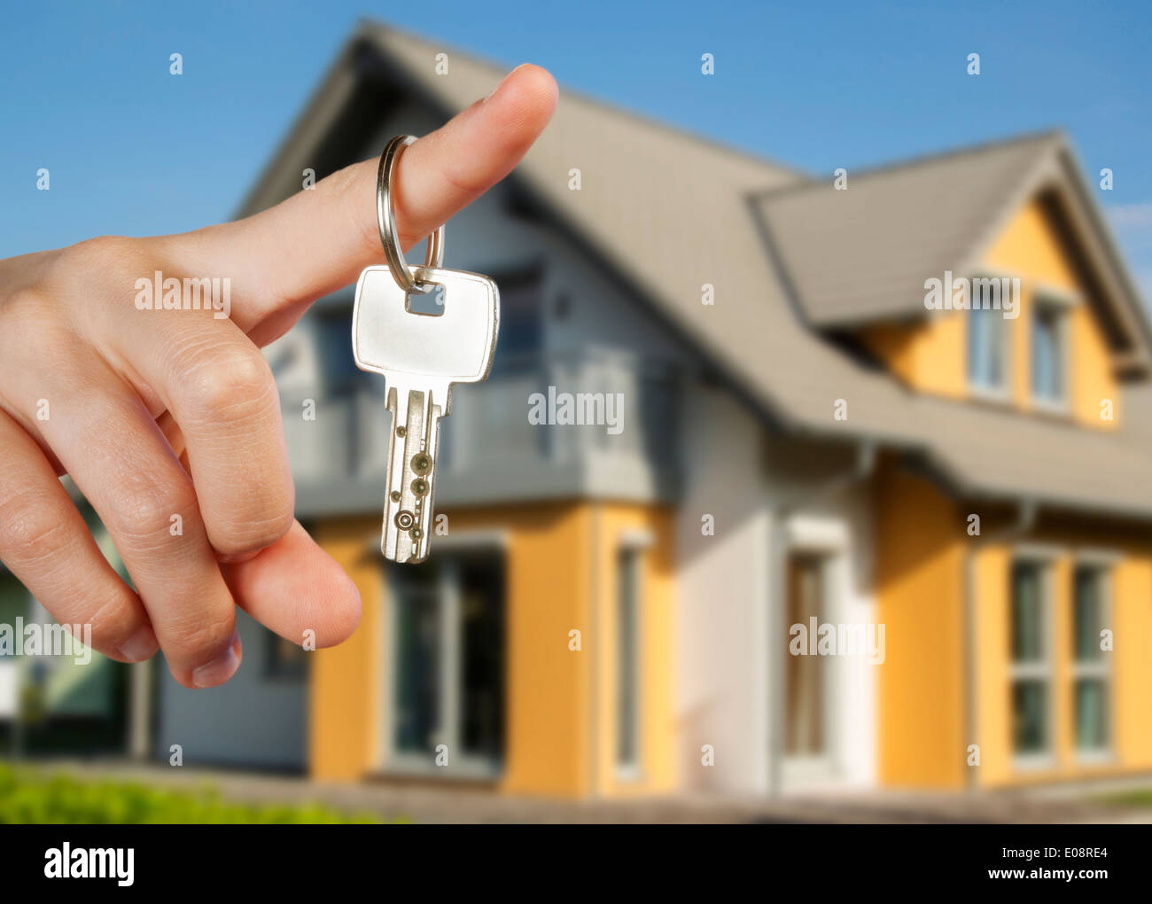 Hand mit Schlüsseln und einem Einfamilienhaus im Hintergrund. Stockfoto