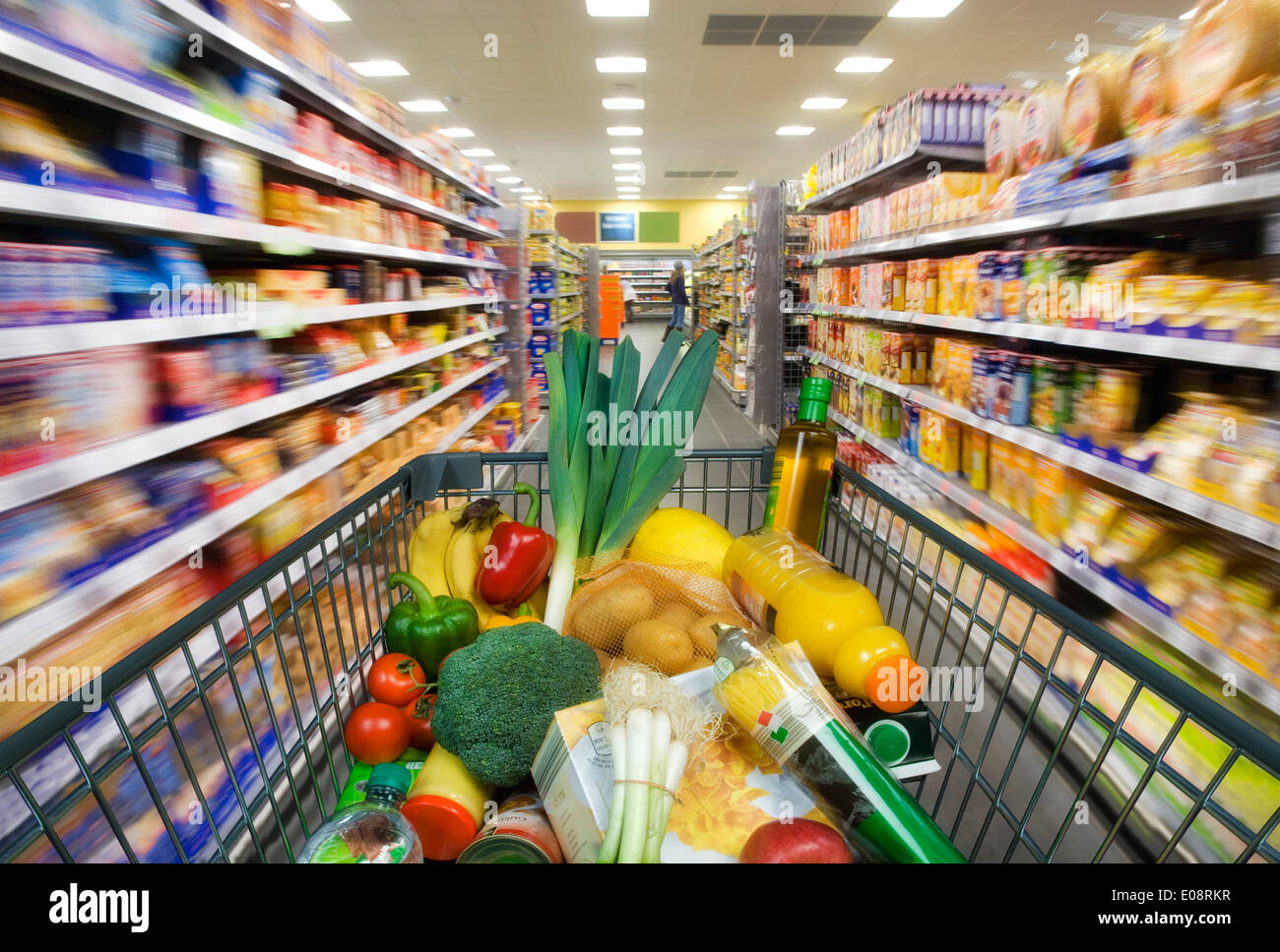 Warenkorb mit Lebensmitteln zwischen den Regalen im Supermarkt. Stockfoto