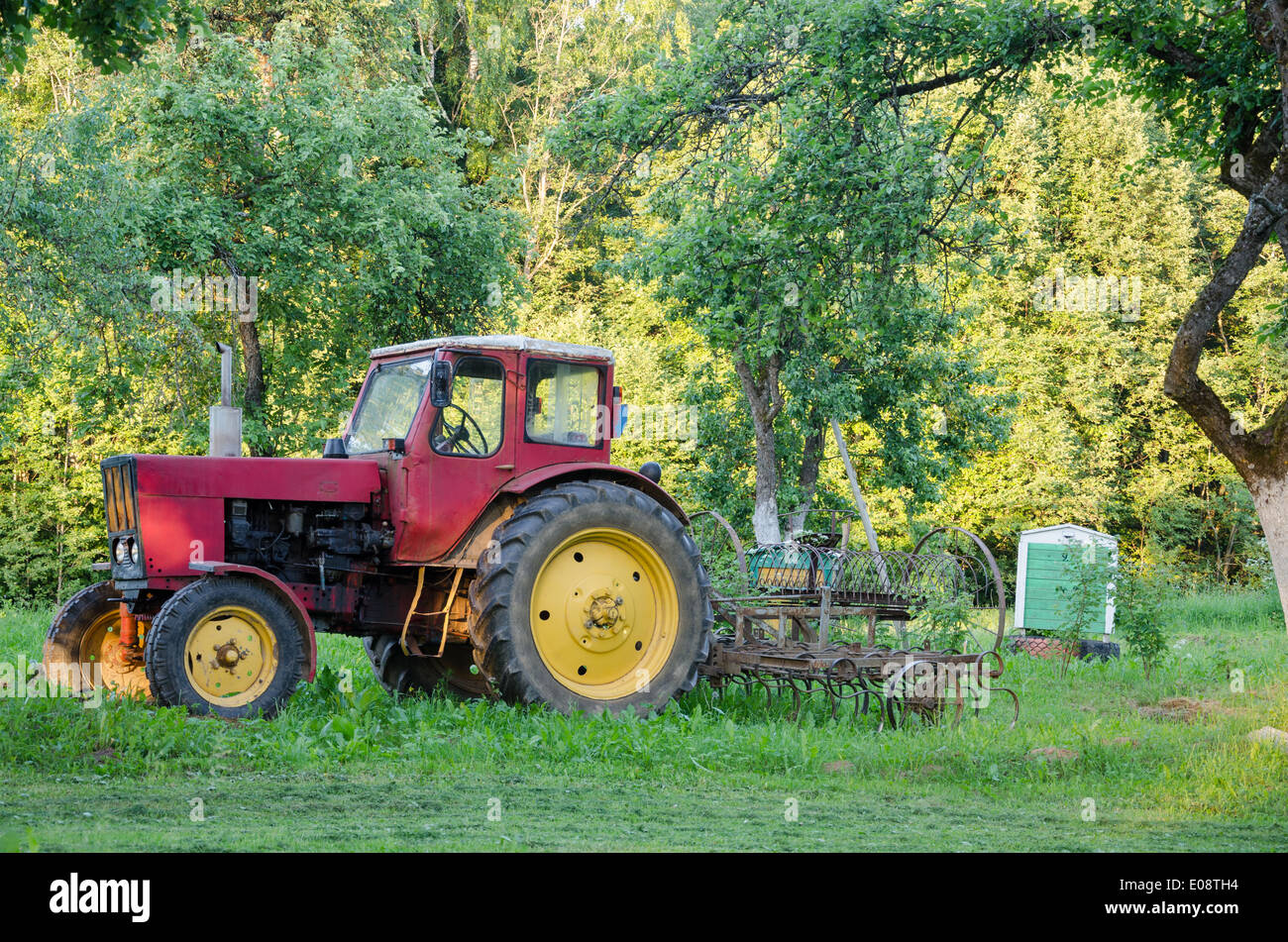 rustikale alte Ackerschlepper mit gelben Rädern und Harow in Gartengras Stockfoto