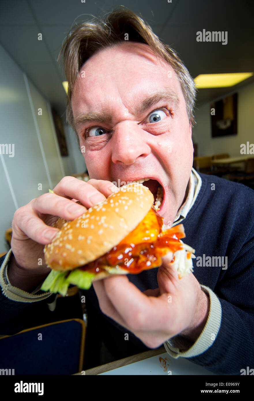 Ein Mann aggressiv in einen Burger beißen. Einen Burger Essen Stockfoto