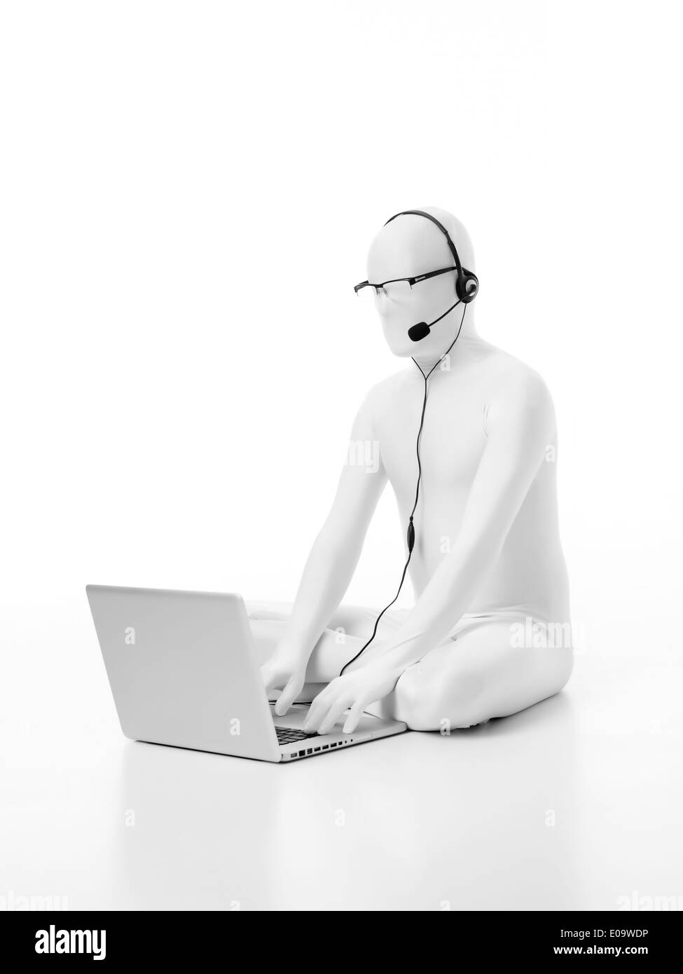 der Mann ohne Gesicht in weiß mit einem Laptop Kopfhörer Mikrofon Kopf und Auge Brille arbeiten auf dem Boden sitzend gekleidet Stockfoto