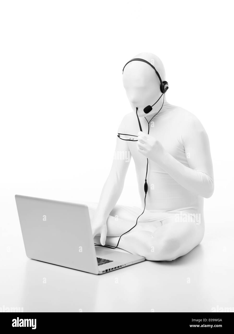 gesichtslose Mann gekleidet in weißen sitzen auf dem Boden mit einem Laptop Kopfhörer Mikrofonkopf und Brille Stockfoto