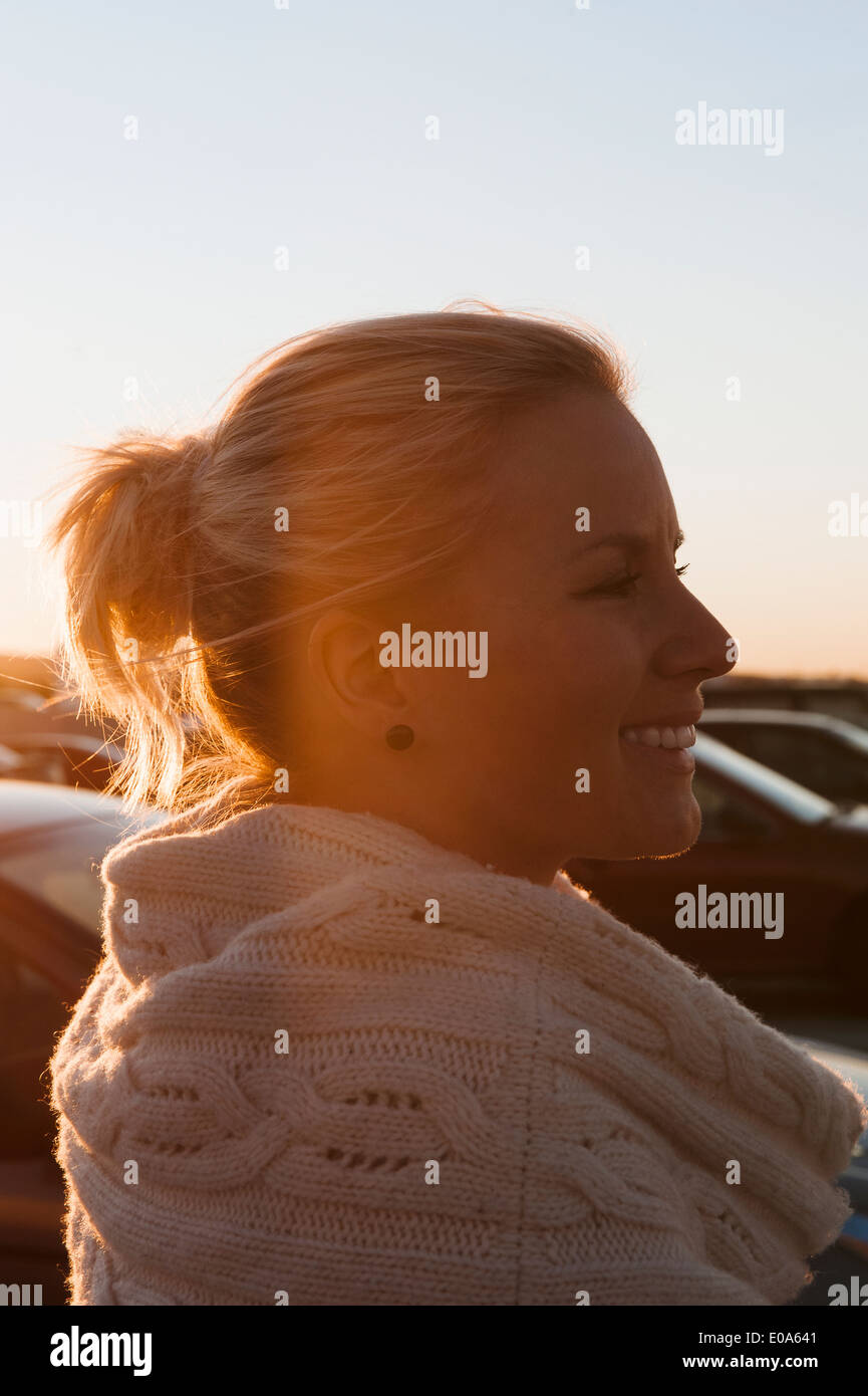 Lächelnde Mitte Erwachsene Frau auf Parkplatz bei Sonnenuntergang Stockfoto