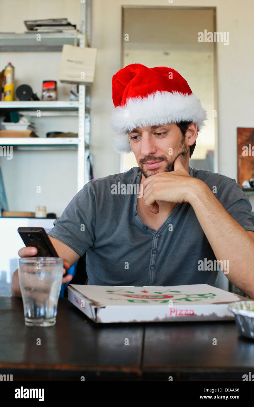 Porträt von Mitte erwachsenen Mann trägt Weihnachtsmütze Blick auf Handy Stockfoto