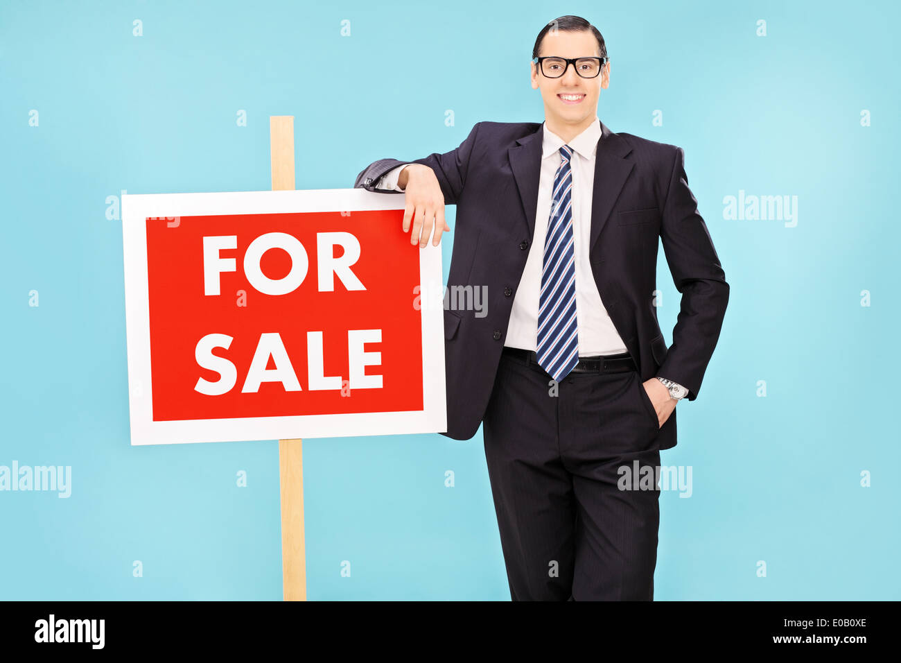 Unternehmer, die neben einem für Verkauf Zeichen auf blauem Hintergrund Stockfoto
