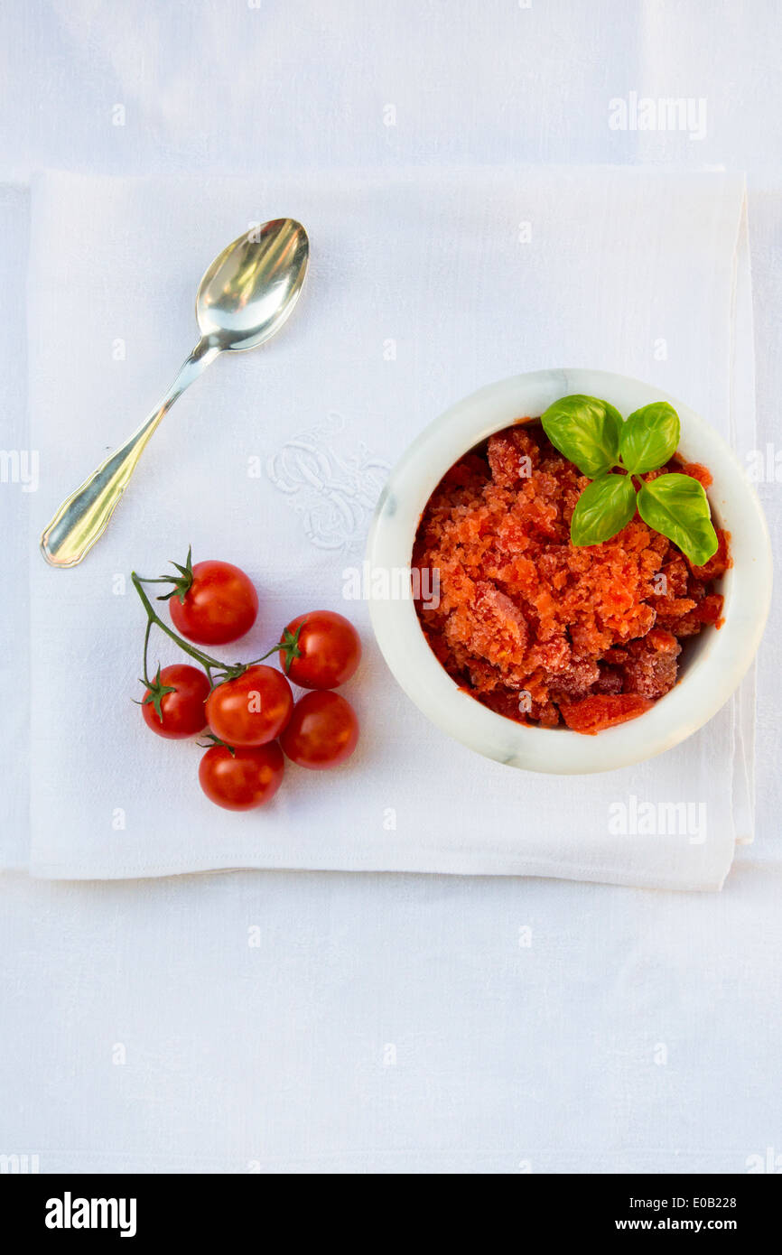 Marmor Schüssel Tomaten Granita garniert mit Basilikum, Tee-Löffel und Cherry-Tomaten auf dem weißen Tuch, Ansicht von oben Stockfoto