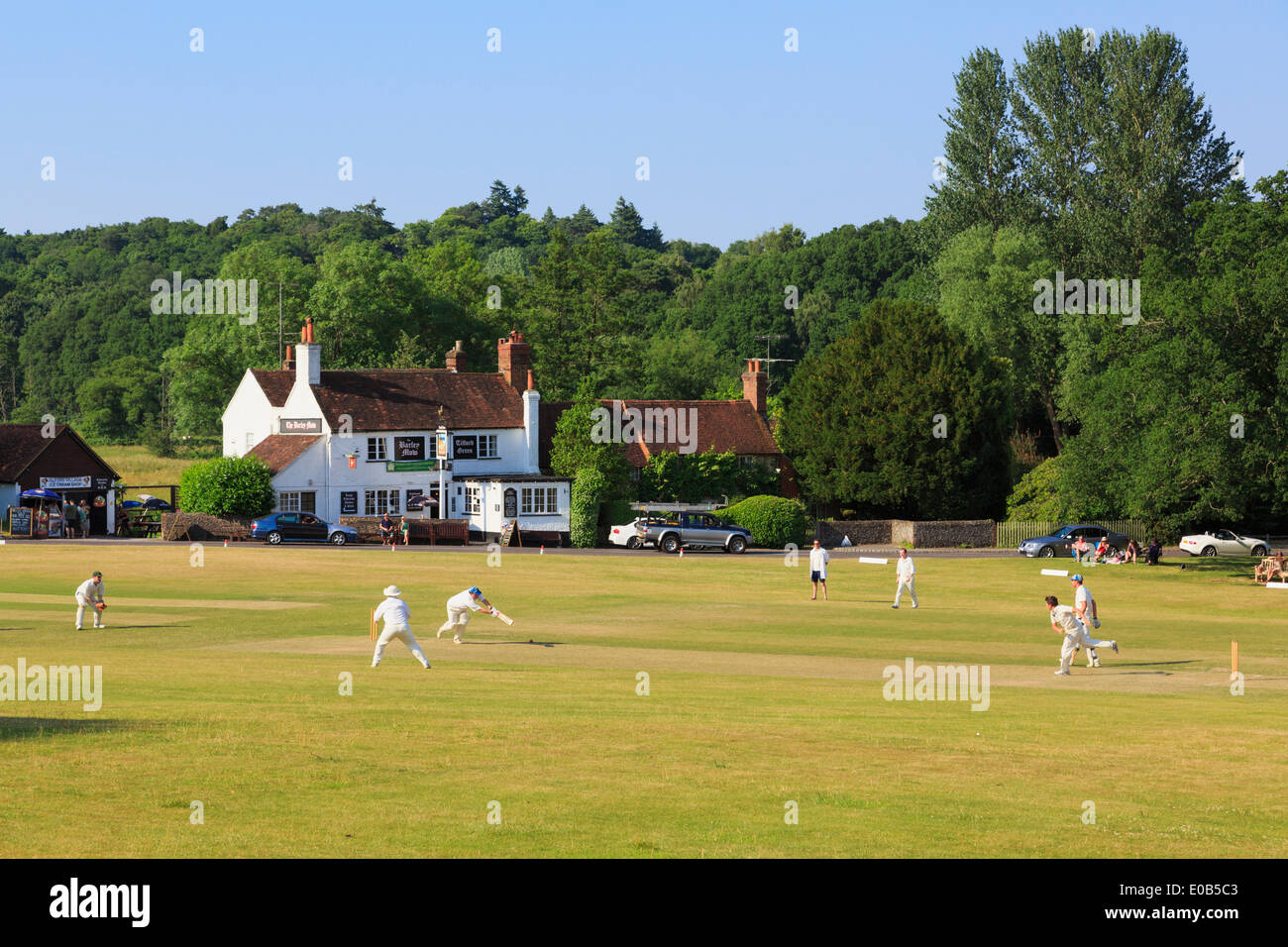 Lokale Teams spielen ein Cricket Spiel am Dorfanger vor Gerste Mähen Pub an einem Sommerabend. Tilford Surrey England UK Stockfoto