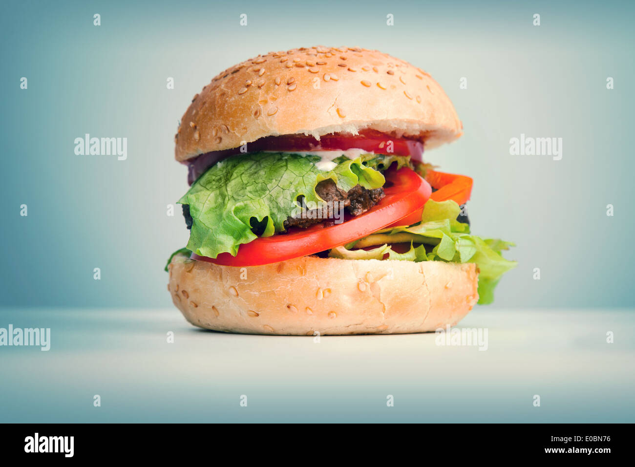 Großen Hamburger liegt auf dem Tisch vor blauem Hintergrund, getönten Retro Foto Stockfoto