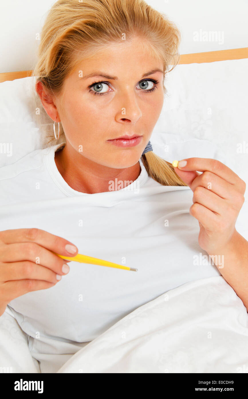 Eine Frau im Bett ist krank und hat Fieberthermometer., Eine Frau Im Bett ist Krank Und Hut Fieberthermometer. Stockfoto