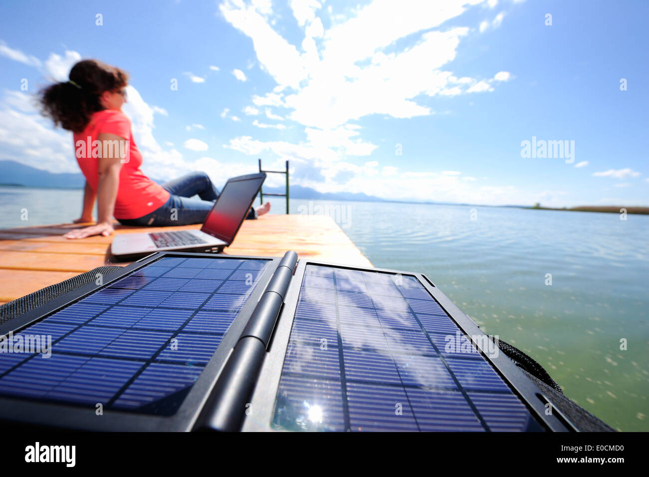 Frau sitzt auf einem Steg am See Chiemsee, Laptop und Solar-Panel im Vordergrund, Chiemgau, Upper Bavaria, Bavaria, Germany Stockfoto