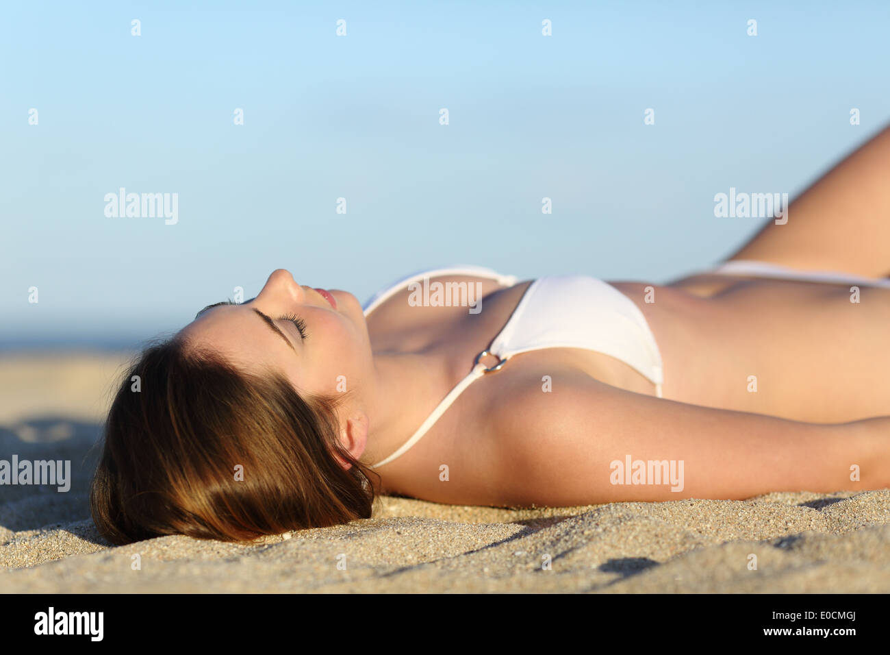 Schöne Frau, Sonnenbaden am Strand mit dem Himmel im Hintergrund liegenden Stockfoto