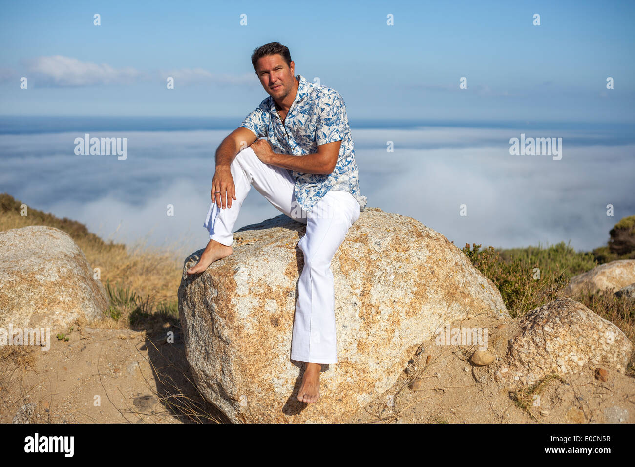 Weißer Mann sitzt auf einem Felsen in der Natur auf einem Berg über den Wolken Stockfoto