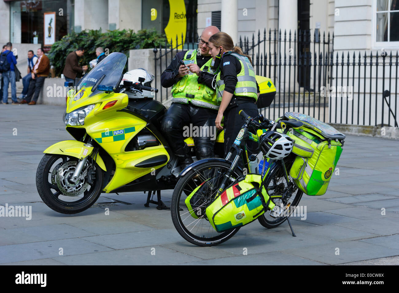 Zwei Sanitäter SMS am Telefon durch ein high-Speed-Motorrad und ein Fahrrad in der Stadt von London, England, Vereinigtes Königreich. Stockfoto