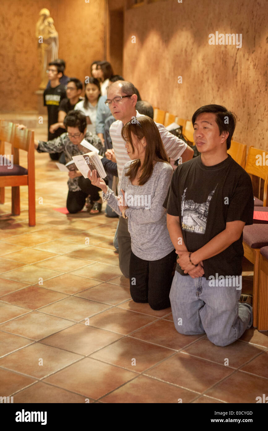 Asiatische Gemeindemitglieder Knien im Gebet während der Messe in der St. Timothy katholische Kirche, Laguna Niguel, CA. Hinweis Frau liest die Stationen des Kreuzes im Rahmen der feierlichen Liturgie des Karfreitags. Stockfoto