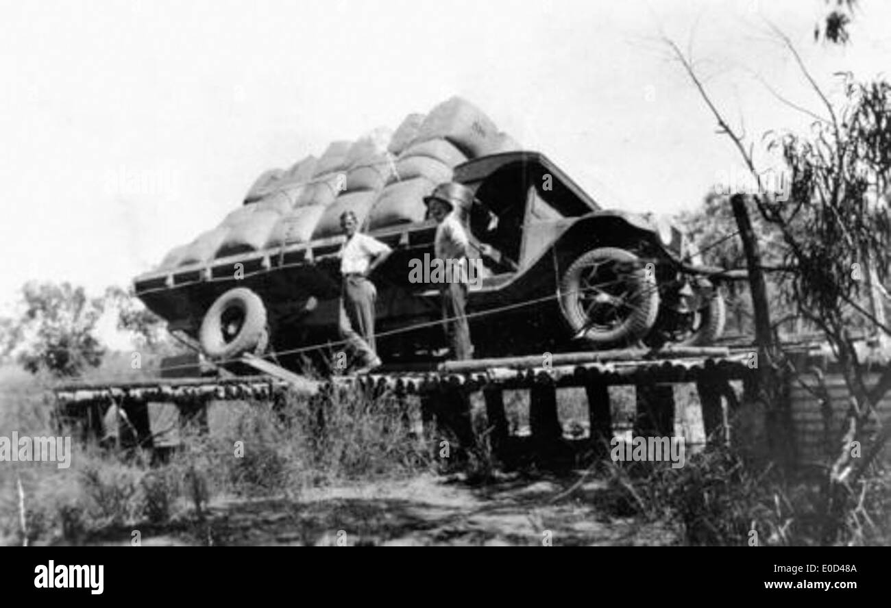 Dieses Bild zeigt einen umgekippten internationalen Lkw auf einer Holzbrücke, der eine große Ladung Wollballen transportiert. Der Unfall des Lkws verdeutlicht die Herausforderungen des Verkehrs und der Infrastruktur des frühen 20. Jahrhunderts. Stockfoto