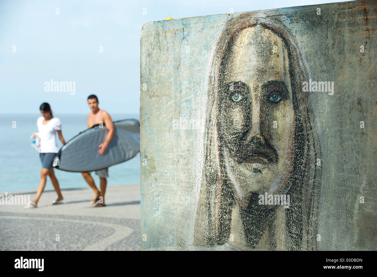 Brasilianer zu Fuß mit Surfbrett in Rio vorbei an brasilianischen Graffiti zeichnen von Cristo Redentor Christus der Erlöser-Porträt Stockfoto