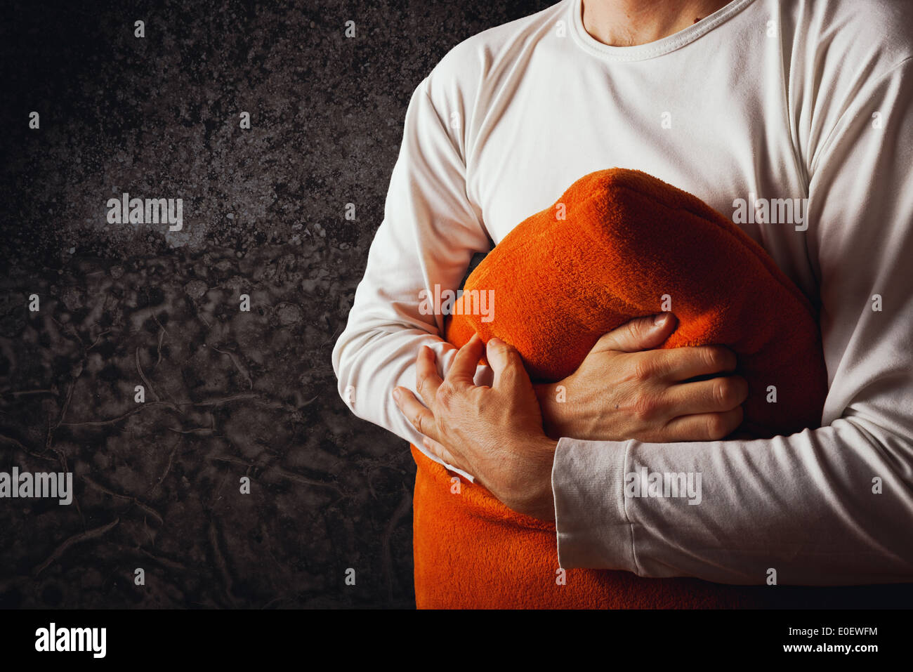 Mann umarmt orange Kissen im dunklen Raum. Konzept von Kummer, Traurigkeit und Depression. Stockfoto