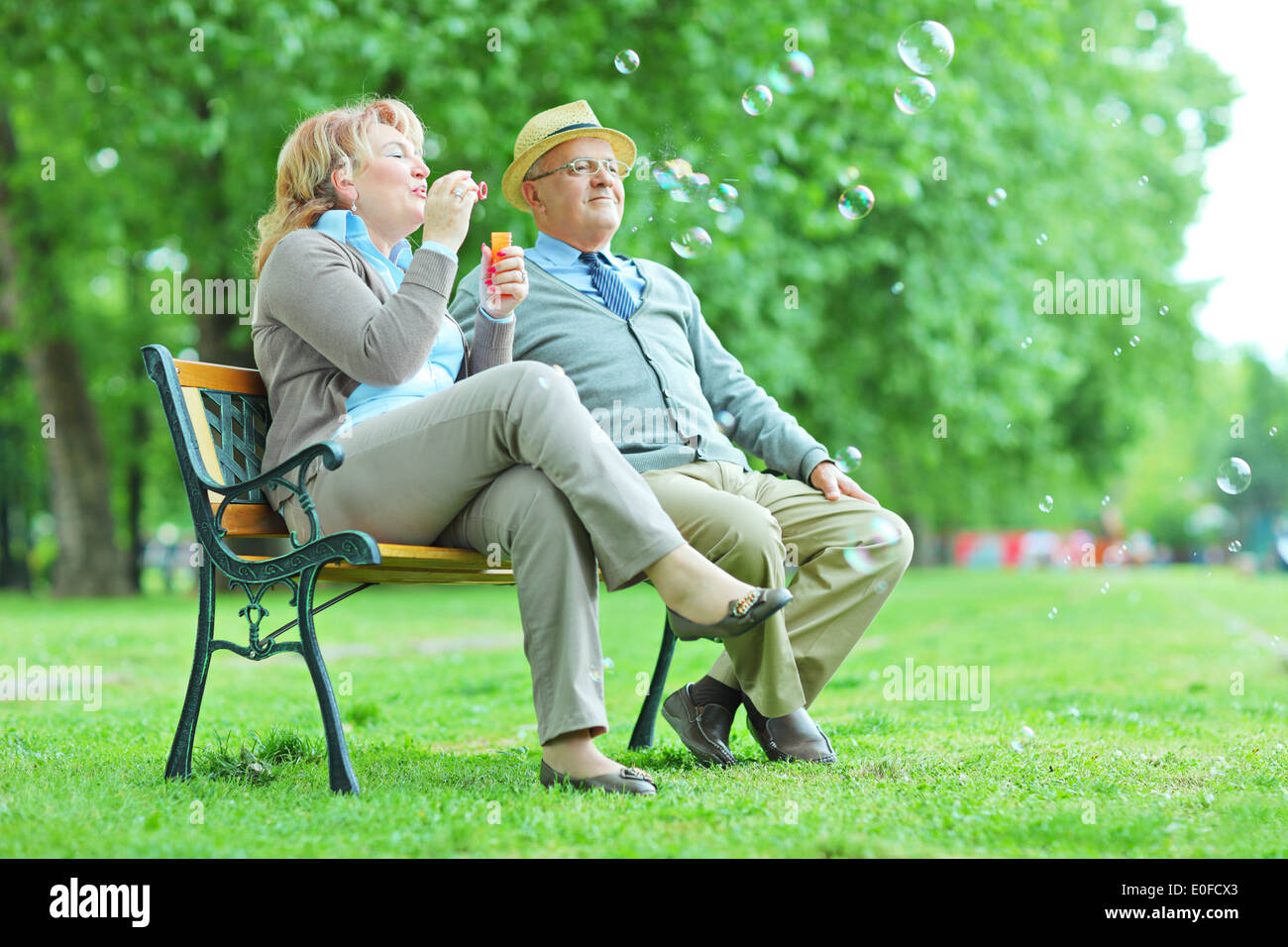 Älteres Ehepaar Seifenblasen im Park sitzend auf Bank Stockfoto
