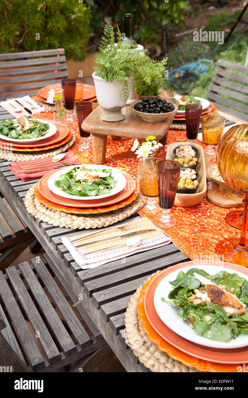 Tischdekoration für Frühjahr Gartenparty mit Spinat auf orange Platten und orangefarbenen  Tischläufer auf Holztisch mit Holzstühlen Stockfotografie - Alamy