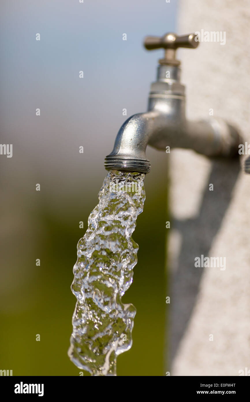 Wasser fließt aus Wasserhahn im Freien an einem sonnigen Tag. Stockfoto