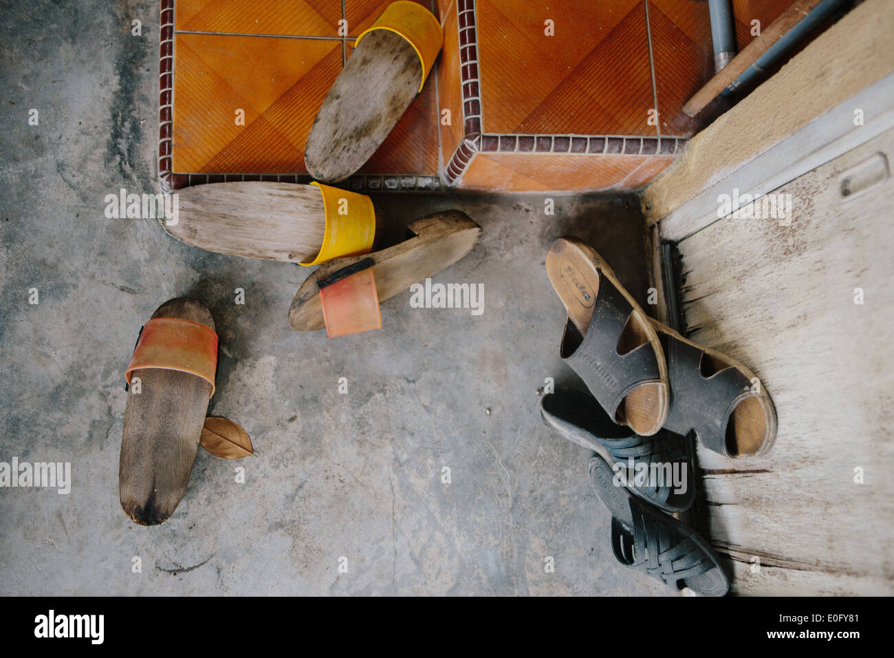 Vier Paar Sandalen in außerhalb eines Hauses mit Orange Holz Fliesen Eingang auf Beton. Stockfoto
